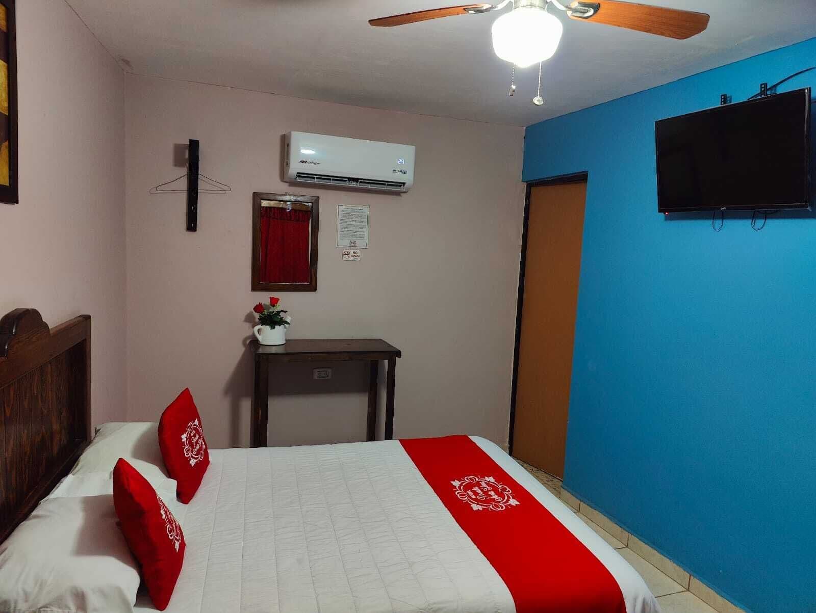 A bedroom with a bed, a ceiling fan, an air conditioner, a TV, and a blue wall.
