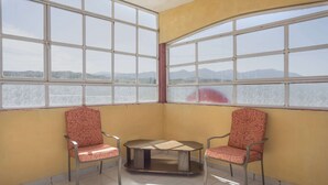 Ein Eckzimmer mit zwei gemusterten Sesseln, einem kleinen Tisch und großen Fenstern mit Blick auf ferne Berge.