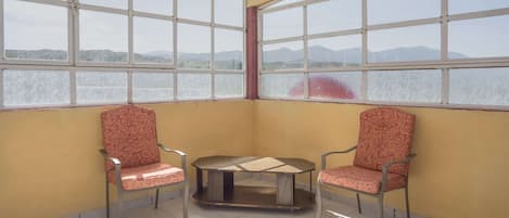 Habitación de esquina con dos sillones estampados, una mesita y ventanas amplias que ofrecen vistas a montañas lejanas.