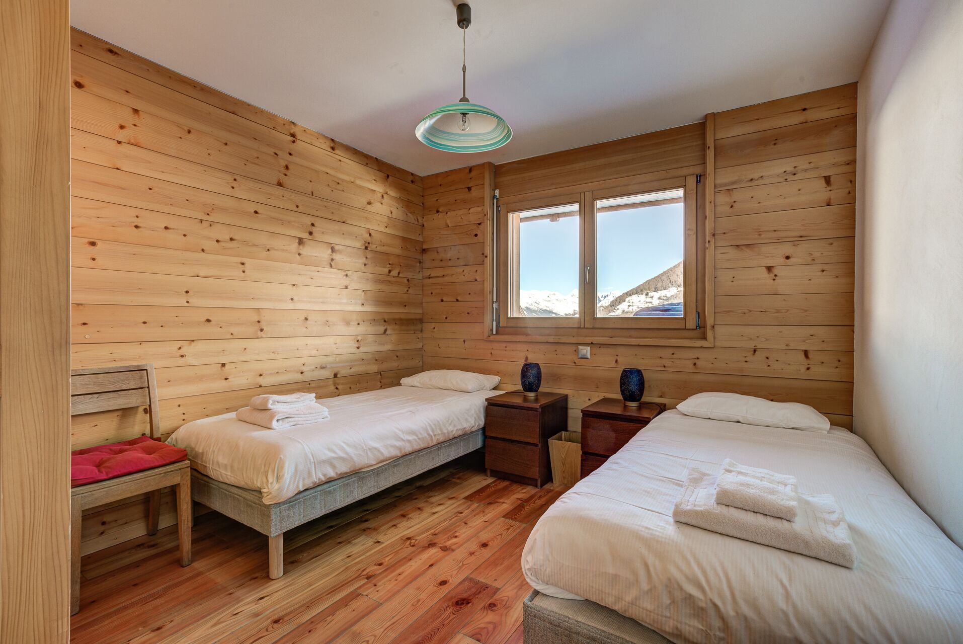 Habitación de cabaña de madera con dos camas, un banco y una ventana que ofrece vistas de montañas nevadas.