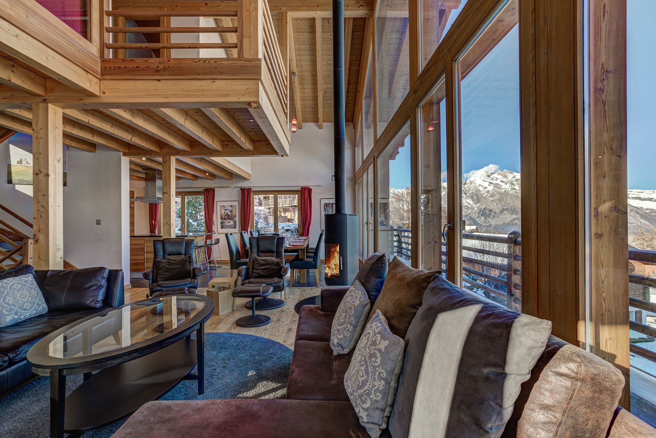 A spacious living area with a large fireplace, wooden beams, and a view of a snowy mountain.