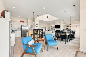 A spacious kitchen with modern appliances, a dining area with blue chairs, and a large TV.