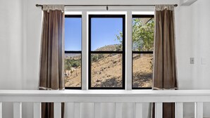 A room with a large window with brown curtains, a white railing, and a view of a dry, hilly landscape. - Lake View and close to Beach (LAKE ISABELLA)