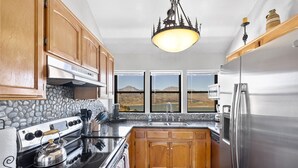 A kitchen with wooden cabinets, a stone backsplash, a stainless steel refrigerator, and a view of mountains through large windows. - Lake View and close to Beach (LAKE ISABELLA)