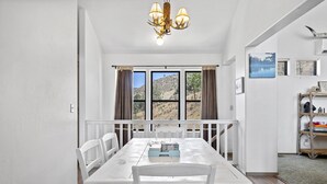 A dining area with a white table and chairs, a chandelier, and a view of a mountainous landscape through large windows. - Lake View and close to Beach (LAKE ISABELLA)