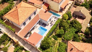 An aerial view of a residential area with terracotta-tiled roofs, a swimming pool, and lush greenery.