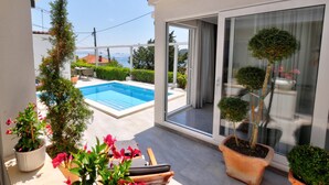 A balcony with a pool, potted plants, and a view of the sea.