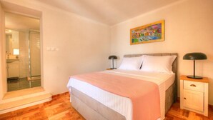 A bedroom with a bed, bedside lamps, a nightstand, a painting on the wall, and a bathroom with a shower.