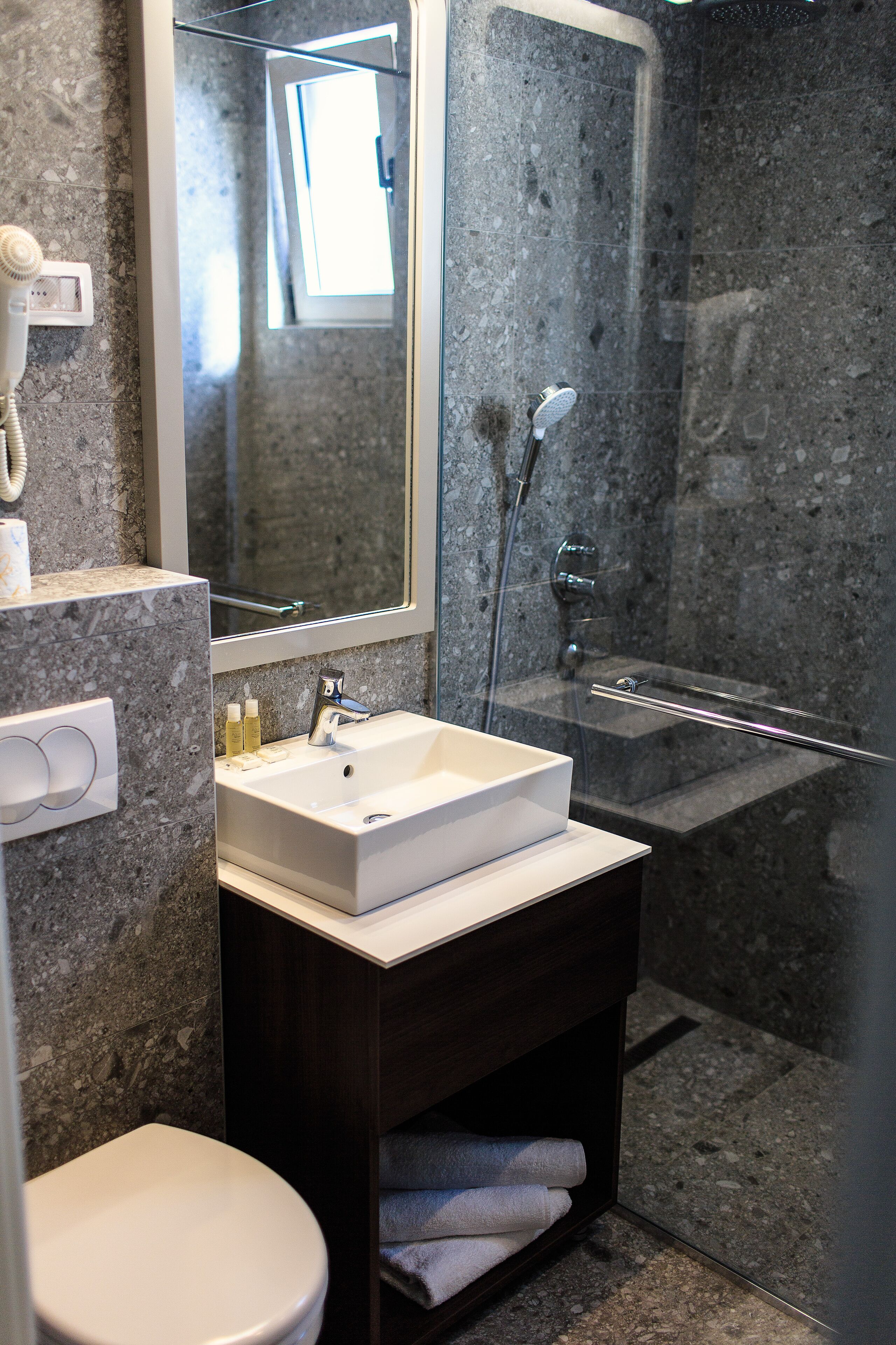 A modern bathroom with a white sink, dark wooden vanity, and a glass-enclosed shower.