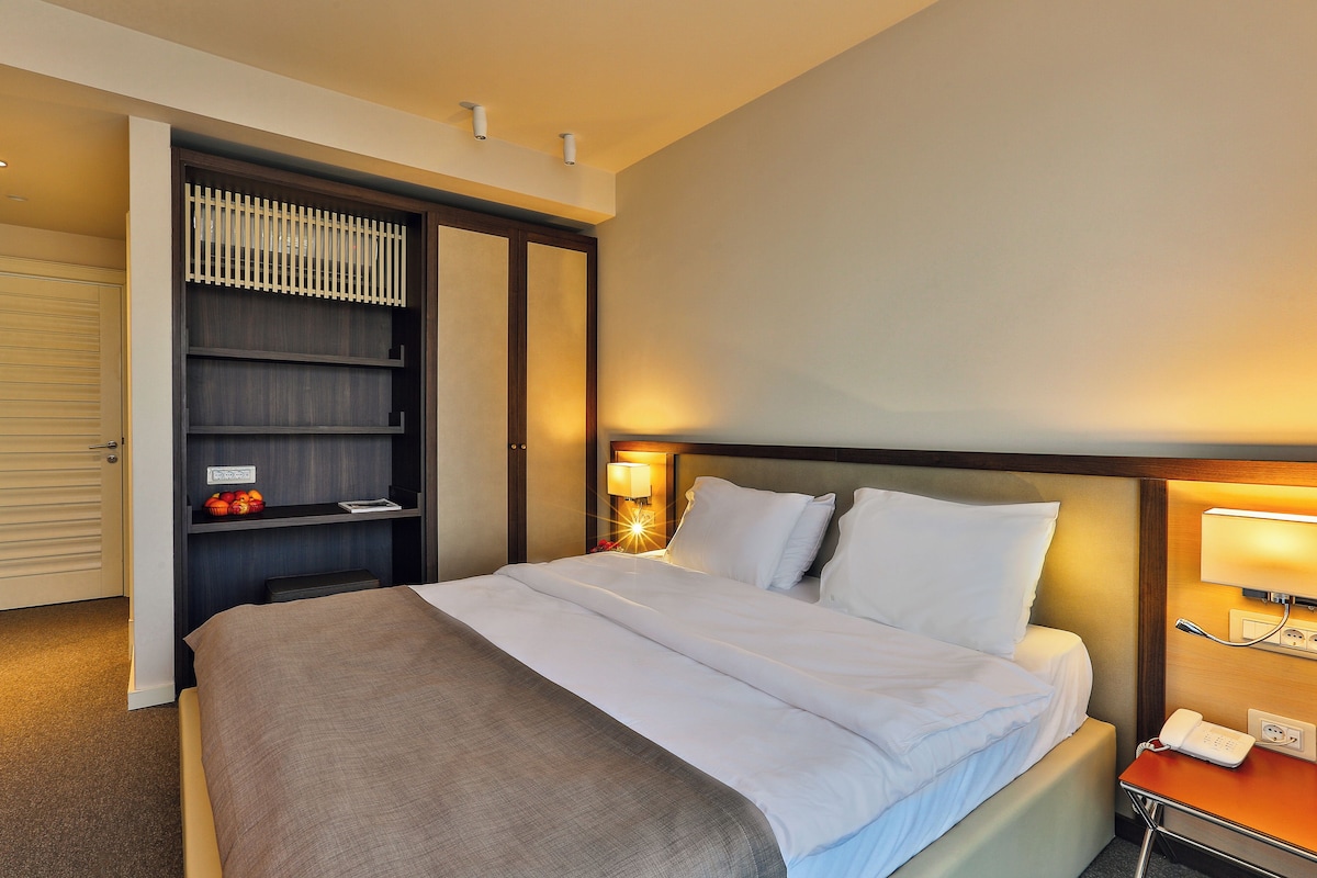 A hotel room with a bed, a wardrobe, a bedside table with a lamp, and a phone.