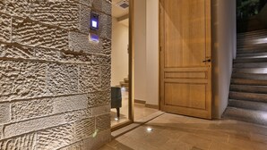 A stone wall with a security camera, a wooden door, and a staircase leading to an upper floor. - Hotel Bono (Becici)