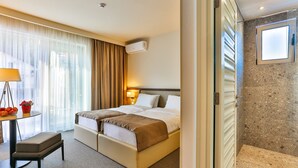 A hotel room with a bed, bedside table, lamp, and a view of the outside through the window. - Hotel Bono (Becici)
