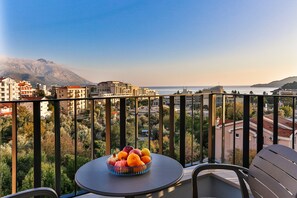 A balcony with a table and chairs, a bowl of fruit, and a view of the sea and buildings. - Hotel Bono (Boreti)