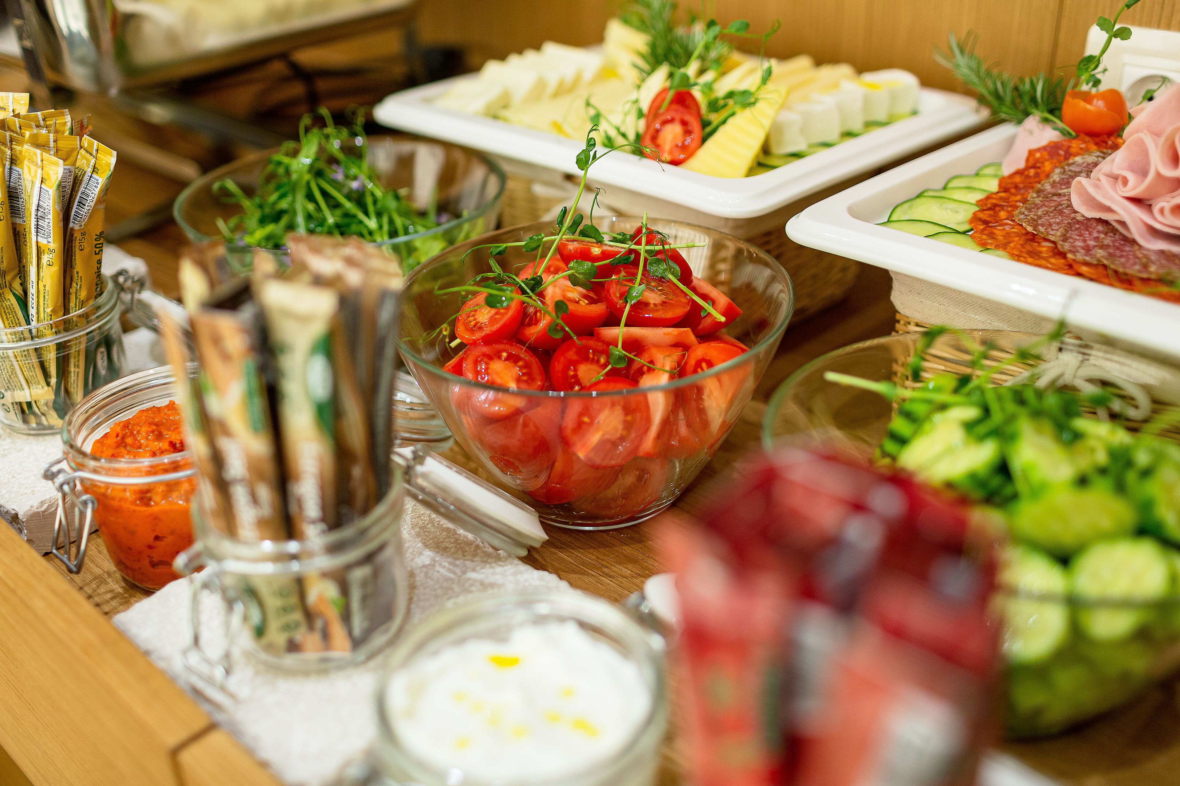 A buffet table with various food items including sliced cucumbers, tomatoes, cheese, and meats.