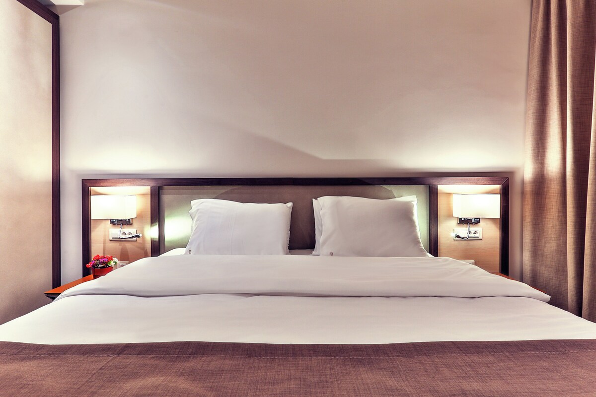 A hotel room with a large bed, two bedside lamps, and a wooden headboard.