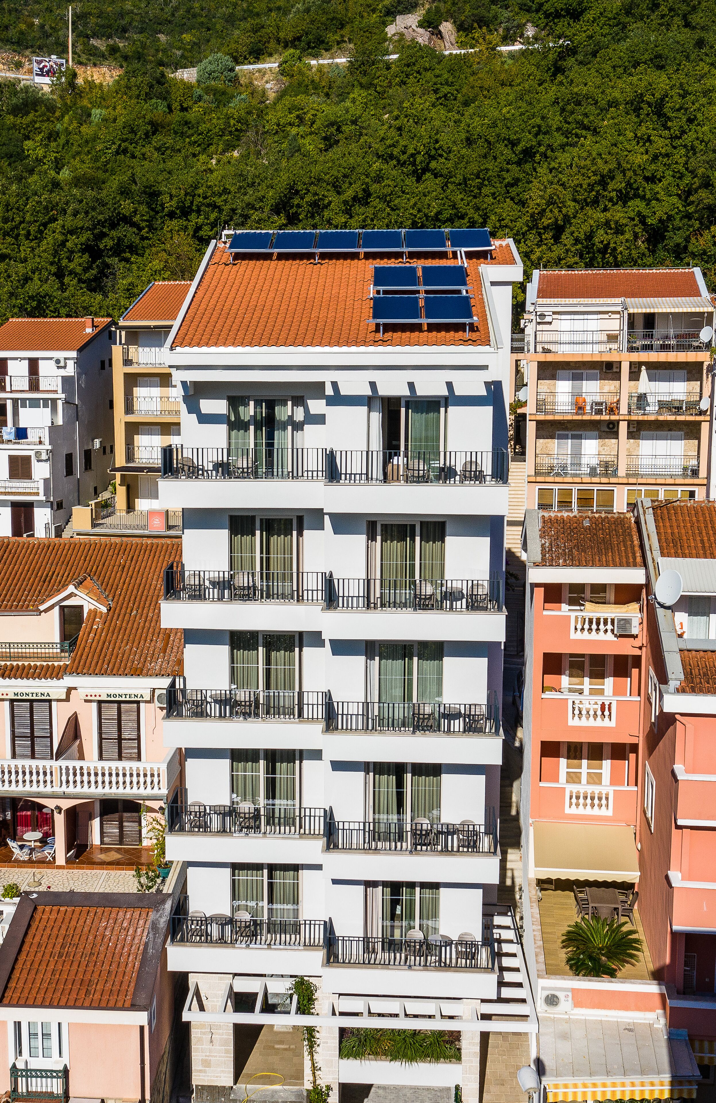 A multi-story building with balconies, solar panels on the roof, and a view of surrounding greenery.