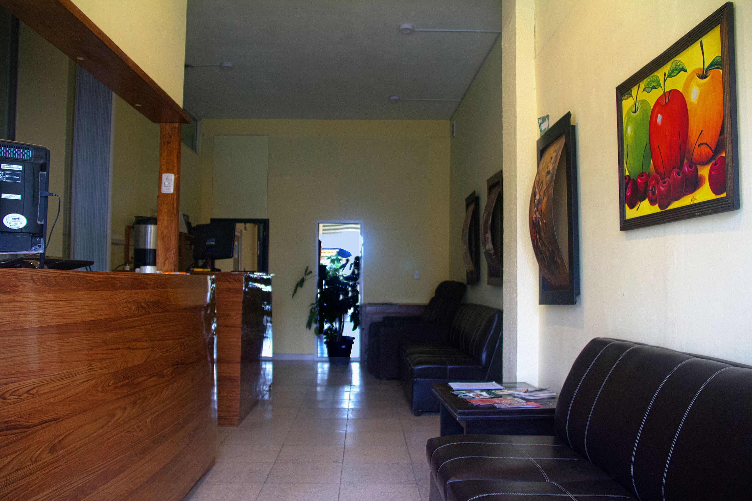 A reception area with a wooden desk, a sofa, and a painting of fruits on the wall.