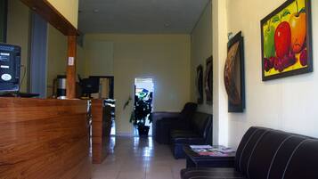 A reception area with a wooden desk, a sofa, and a painting of fruits on the wall.