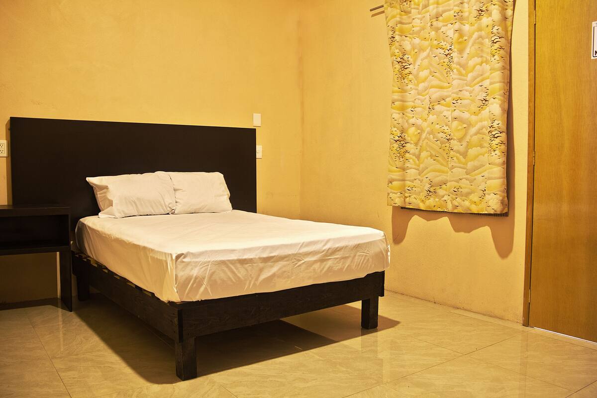 Ein ordentlich bezogenes Bett mit weißer Bettwäsche und Kissen, ein dunkles Holz-Kopfteil und eine Wand mit einem dekorativen Stoffvorhang.