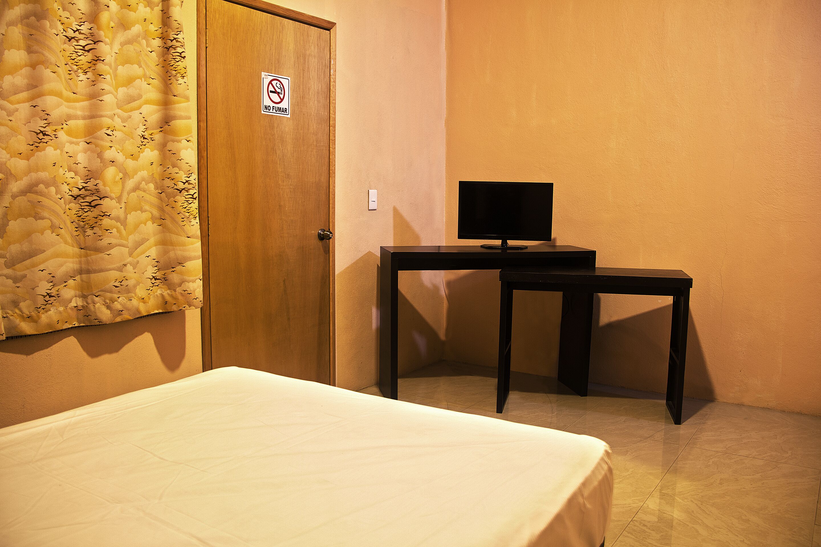 Una habitación de hotel con una cama, un escritorio con una computadora y una puerta con un letrero de 'No Fumar'.