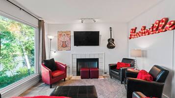 A modern living room with a fireplace, red and black leather sofas, a mounted TV, and a guitar.