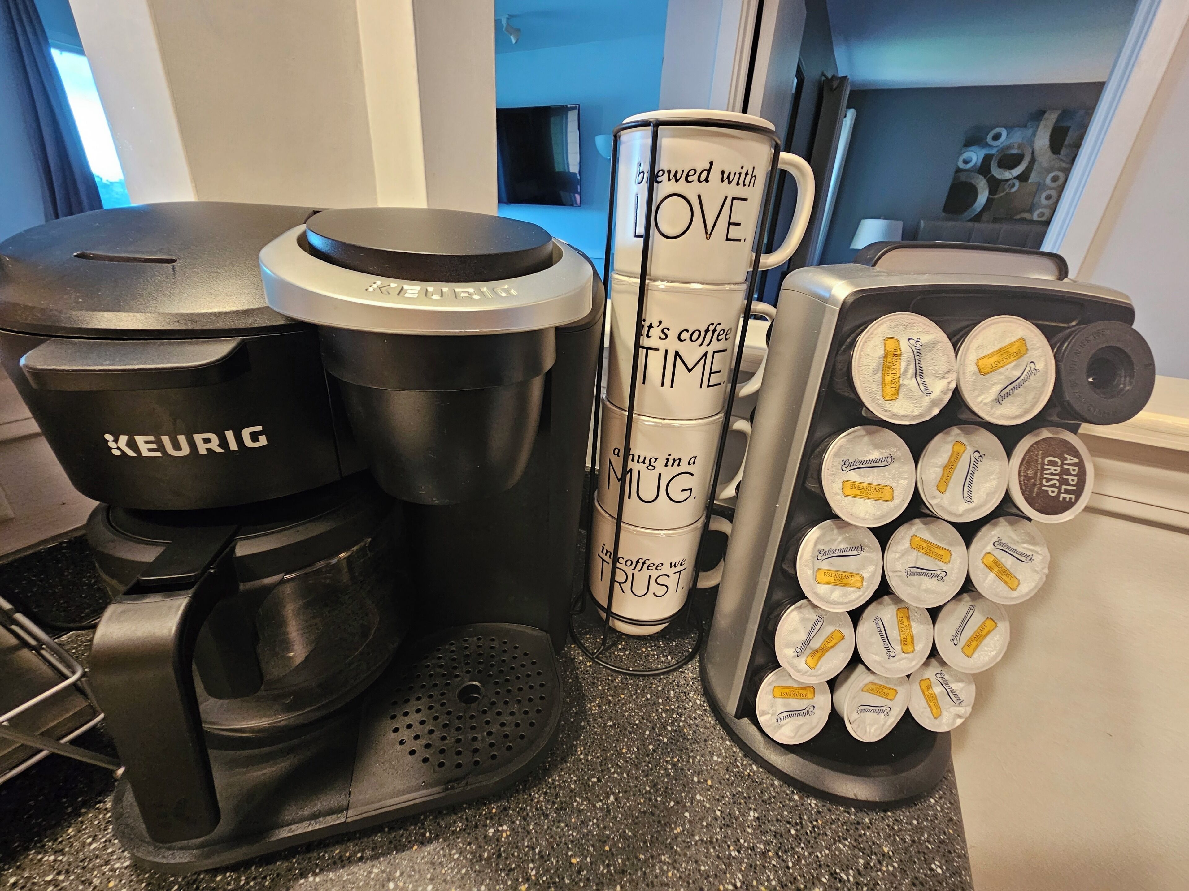 A Keurig coffee maker, a stack of coffee mugs, and a coffee pod dispenser on a kitchen counter.