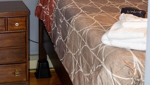 Una camera da letto con un letto, un comodino, una finestra con tende e un quadro appeso al muro.
