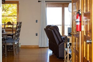 A room with a massage chair, a dining table with chairs, a fire extinguisher, and a window with curtains.