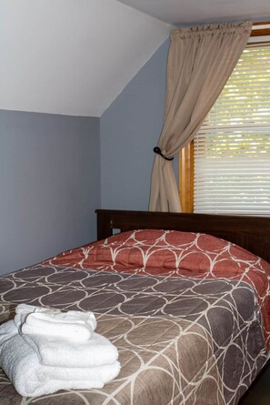 A bedroom with a bed, a window with blinds, and a towel on the bed.