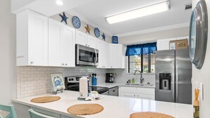 Une cuisine moderne avec des meubles blancs, un réfrigérateur en acier inoxydable et un grand îlot central agrémenté de sets de table en fibres tressées.