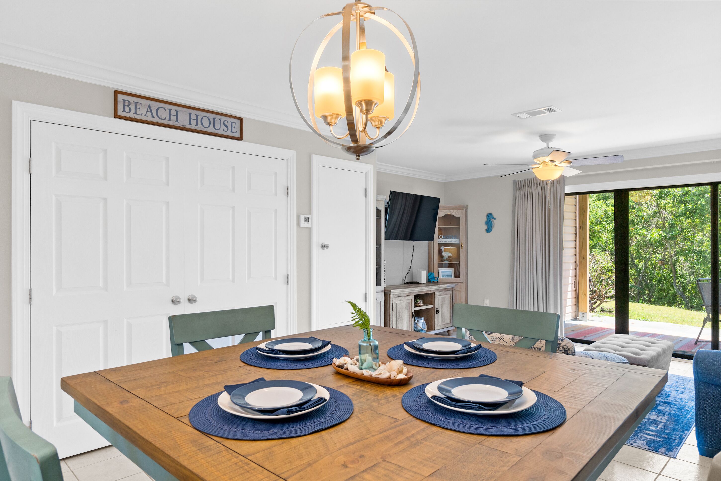 Un comedor con una mesa de madera dispuesta para cuatro personas, una araña y un letrero que dice "BEACH HOUSE".