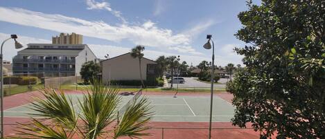 A tennis court with surrounding greenery and buildings in the background.