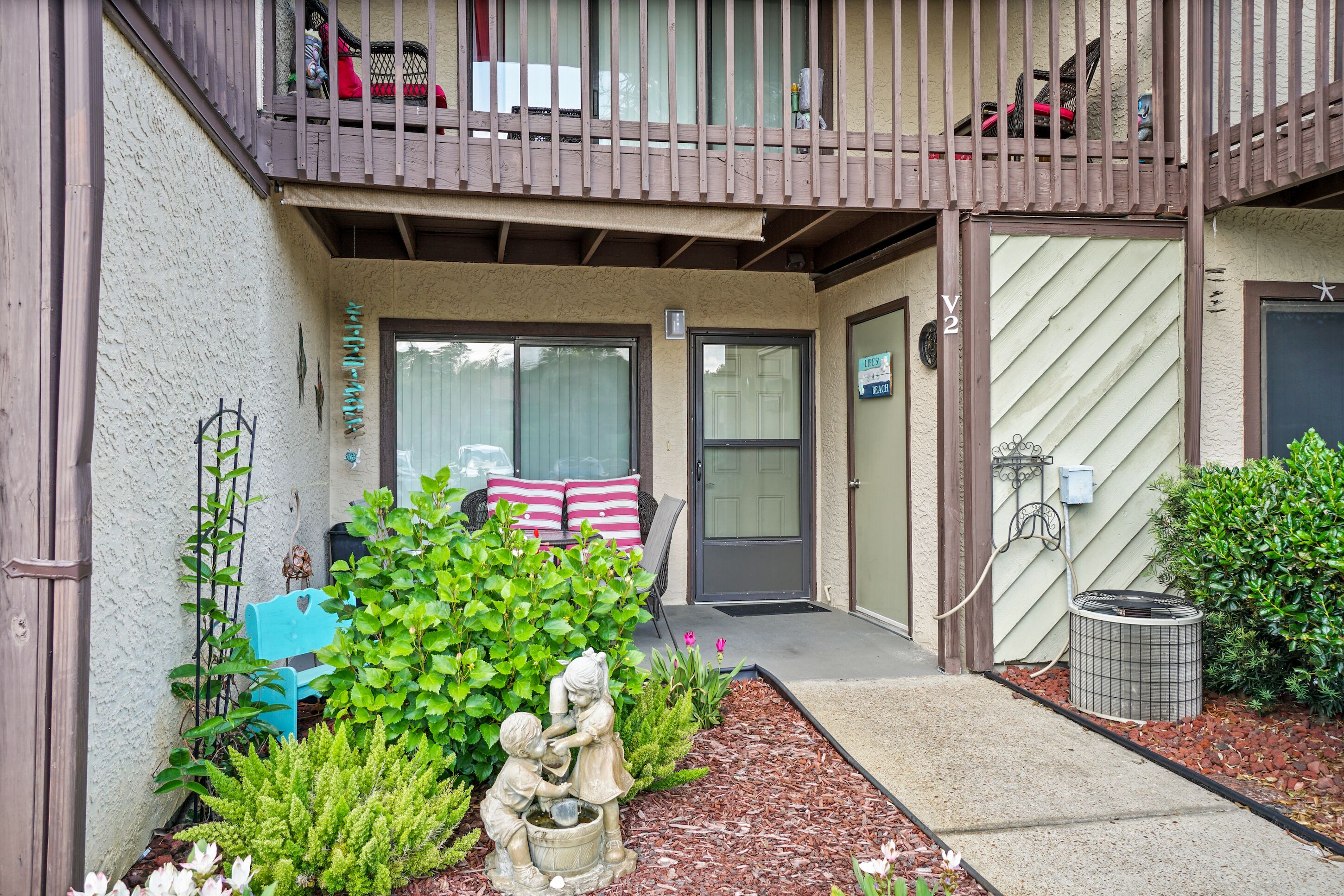 A residential building with a front porch, a mailbox, and a small garden with a statue.