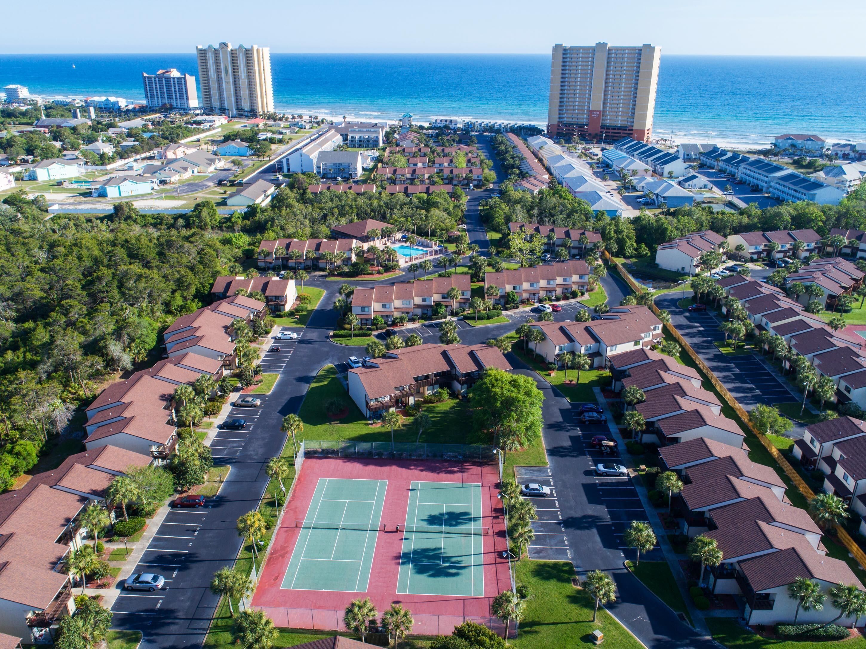 An aerial view of a residential area with multiple-story buildings, a tennis court, and a beachfront.