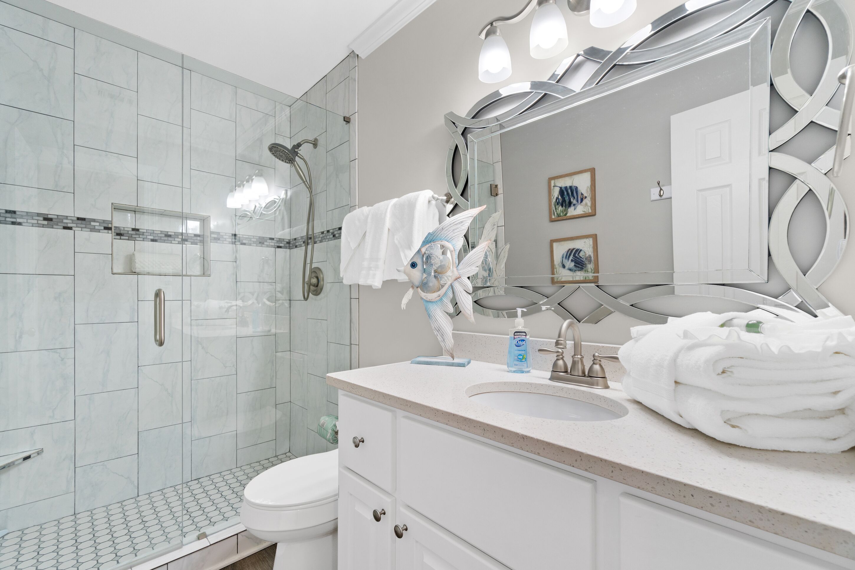 A modern bathroom with a glass shower, white tiles, a vanity with a mirror, and a toilet.