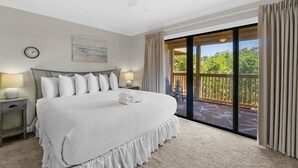 Une chambre avec un grand lit, un ventilateur de plafond, une horloge, une table de chevet et une vue sur un balcon doté d’une balustrade en bois.