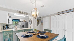 Un coin repas avec une table en bois dressée pour quatre personnes, des chaises de couleur turquoise et un lustre.