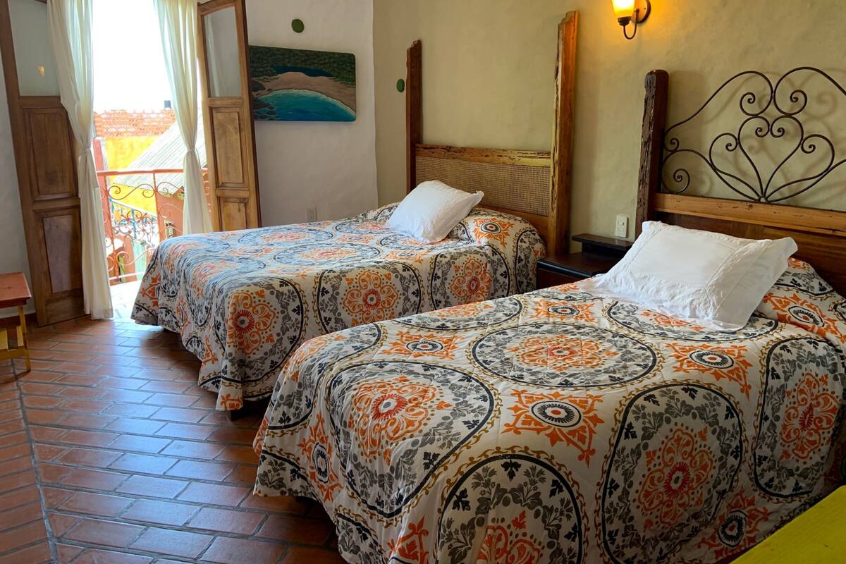 A room with two beds, a painting, a wall-mounted light, and a balcony with a view.