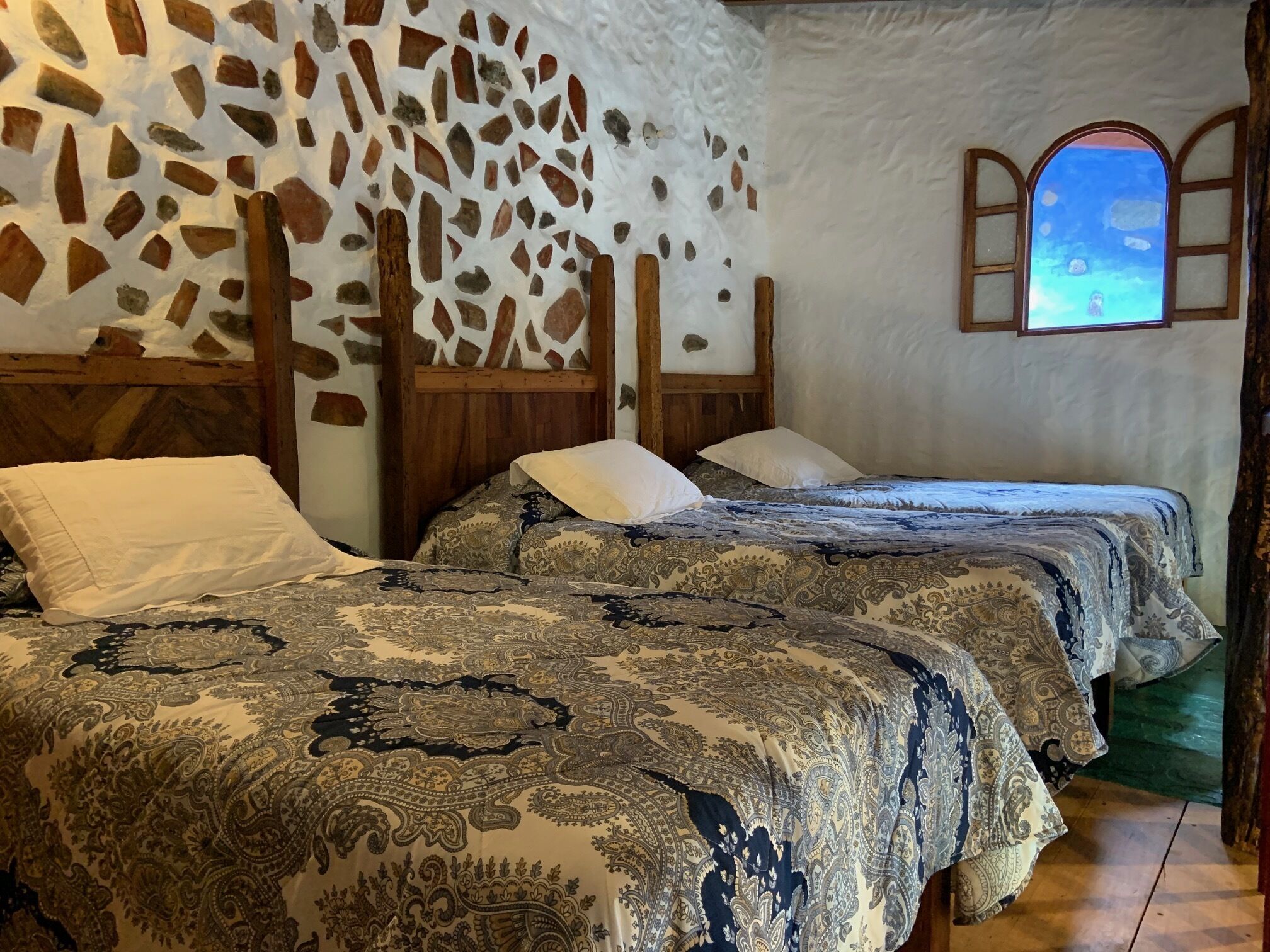 Una habitación con dos camas, una pared de piedra, un cabecero de madera y una ventana con vistas.