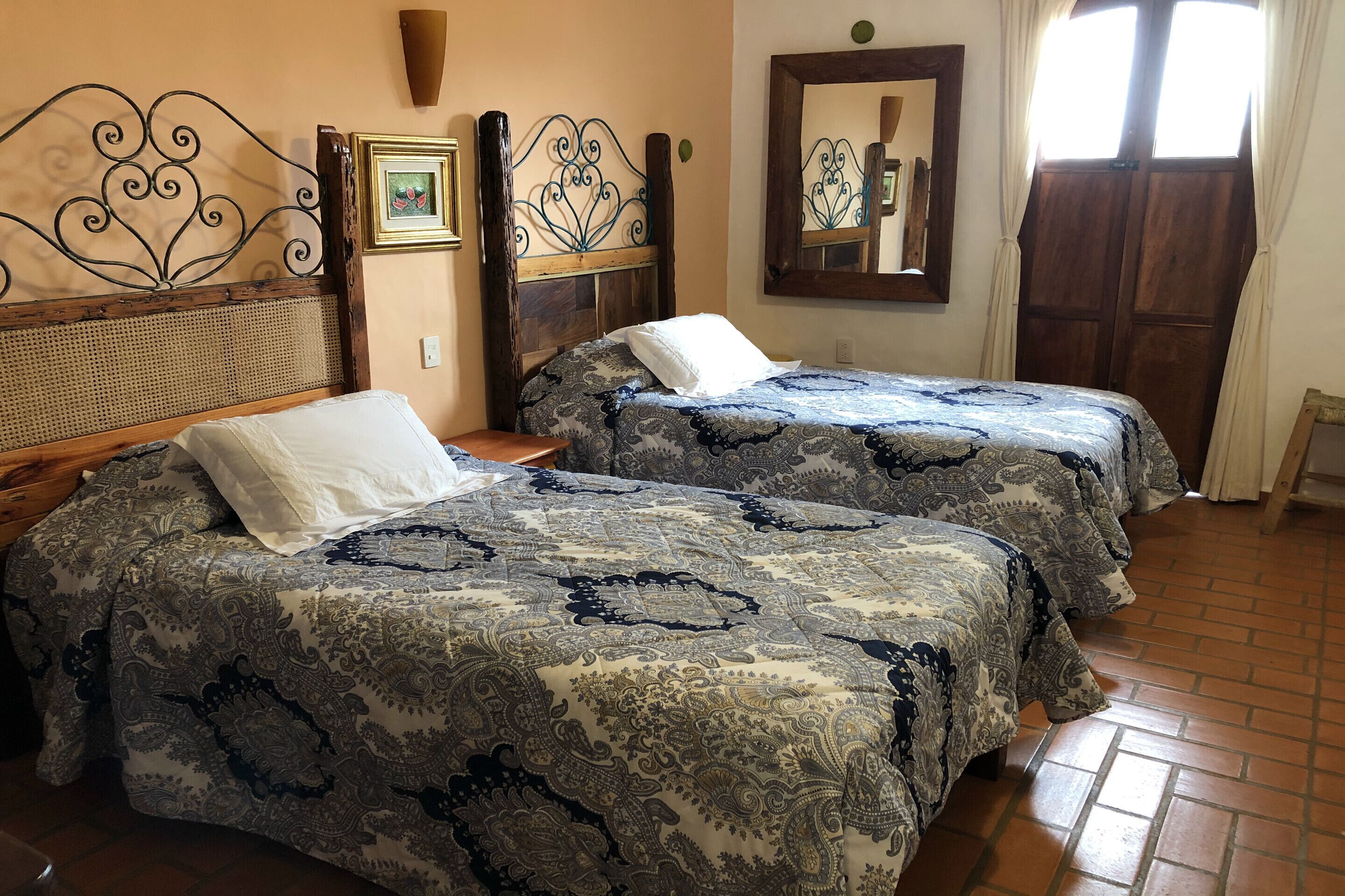 A hotel room with two beds, a wooden headboard, a mirror, and a window with curtains.