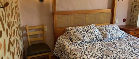 A bedroom with a wooden bed, patterned bedding, a wooden chair, and two wall-mounted lamps.