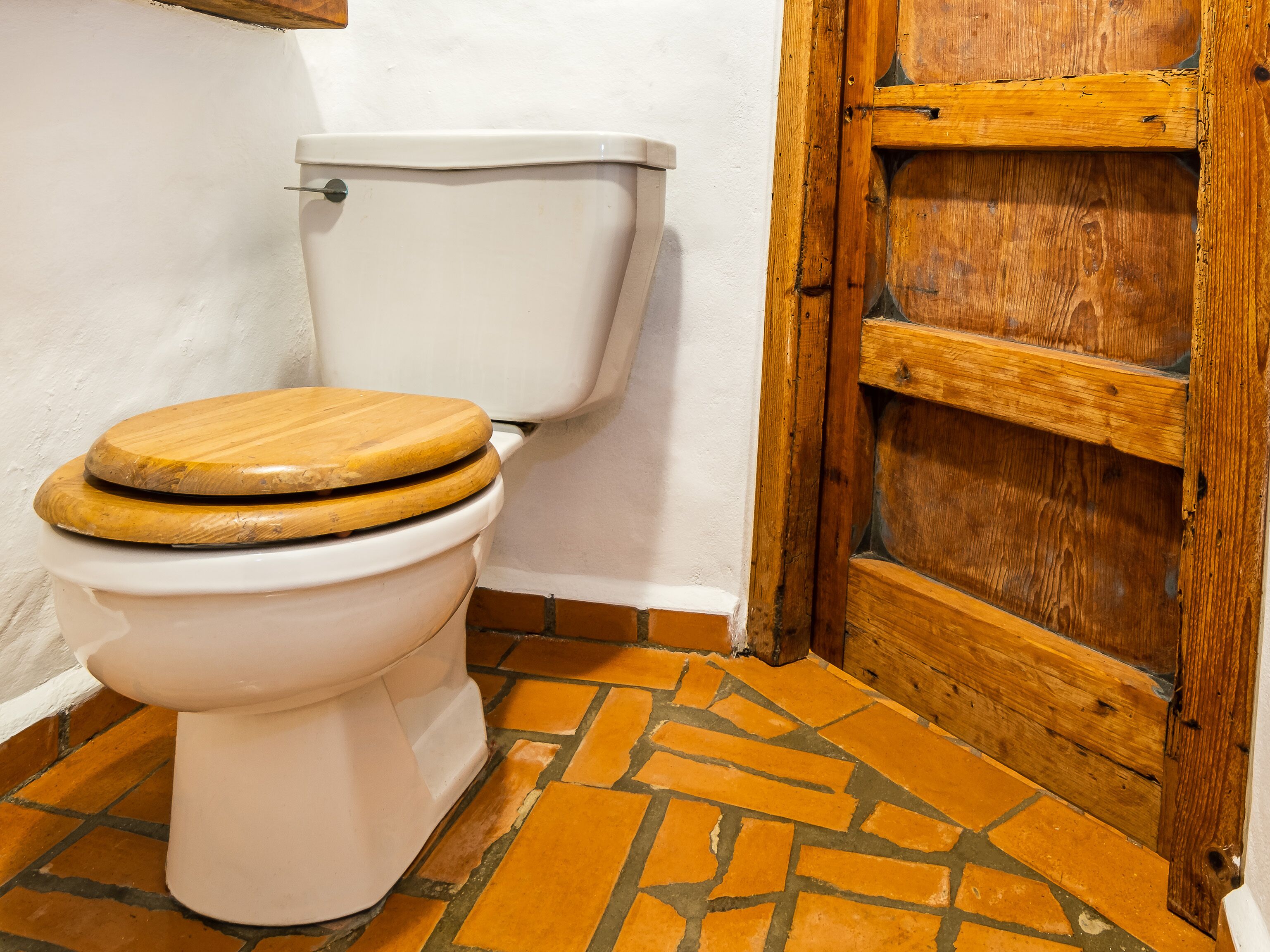 A white toilet with a wooden seat and a tiled floor with geometric patterns.