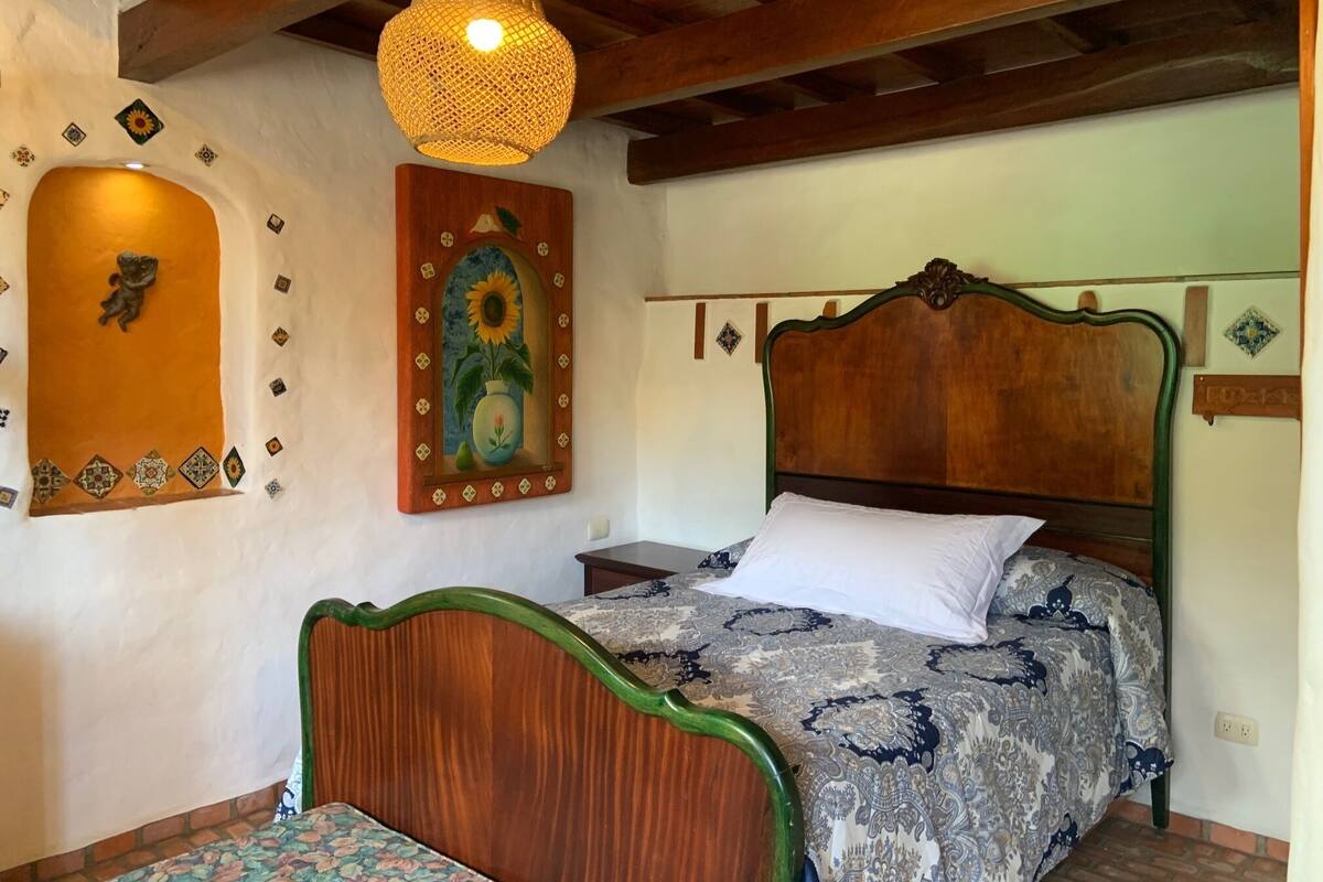 A bedroom with a wooden bed, a patterned bedspread, a hanging light fixture, and decorative wall art.
