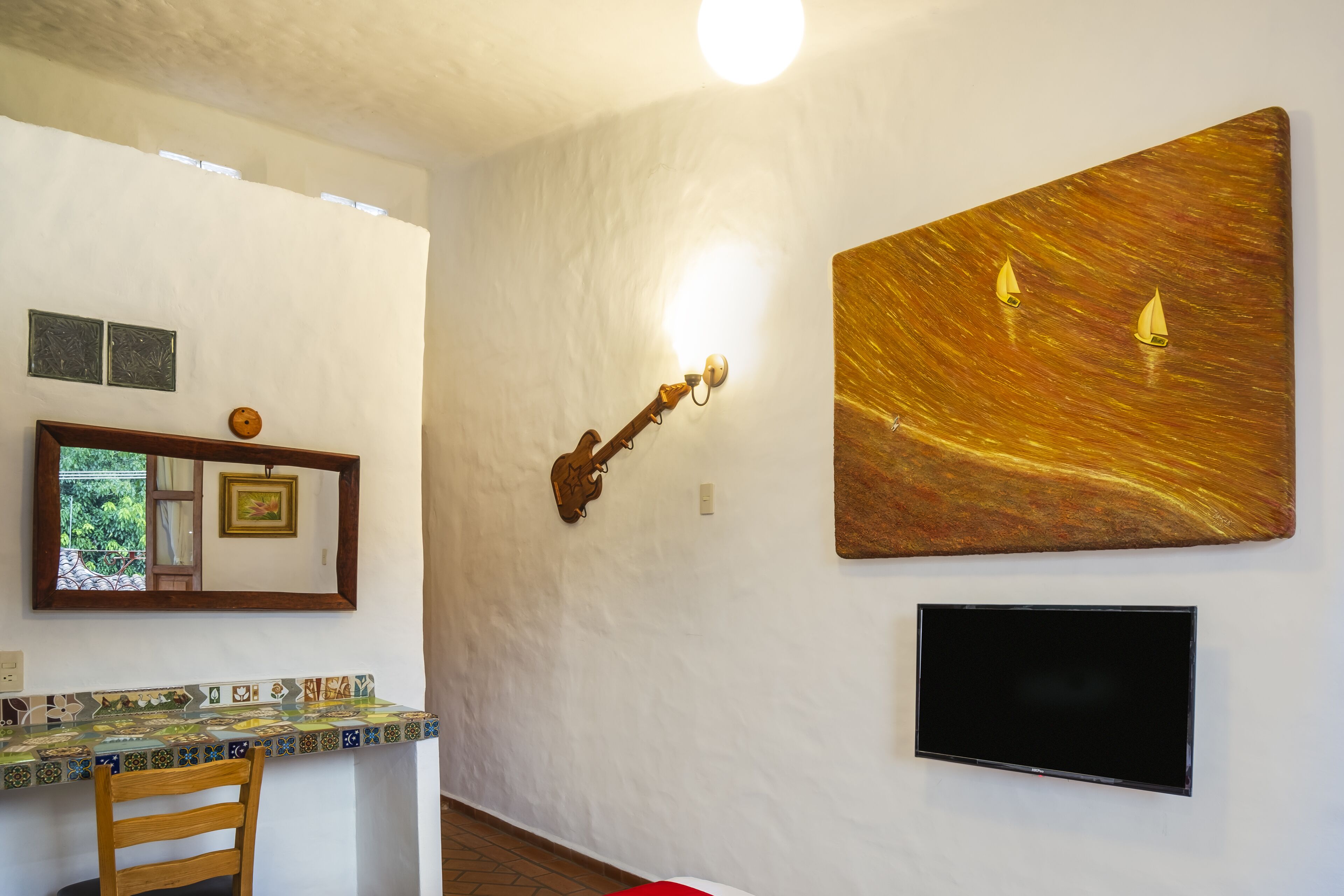 A room with a tiled table, a wooden chair, a guitar wall art, a painting, and a TV.