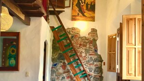 A cozy interior with a wooden staircase, a stone wall, and a painting of dancers. - Casa Miguel Arcangel (Coatepec)