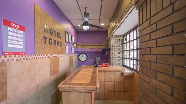 Uma área de recepção de hotel com parede roxa, um relógio, um ventilador de teto e uma janela com vista para o exterior.