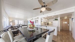A spacious dining area with a long table, several chairs, a ceiling fan, and a kitchen in the background.