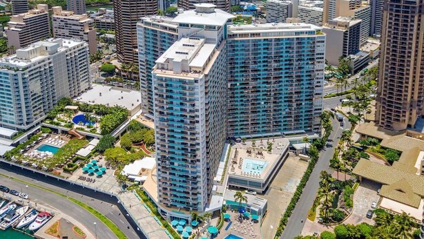 An aerial view of a high-rise hotel with multiple floors, a rooftop pool, and surrounding greenery.