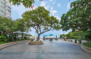 A spacious outdoor area with a large tree, seating arrangements, and a view of a building in the background.
