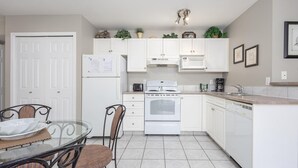 Una cocina compacta con gabinetes blancos, un horno empotrado, un microondas y un lavabo. Hay una mesa de comedor con sillas y una pequeña isla con otro lavabo.